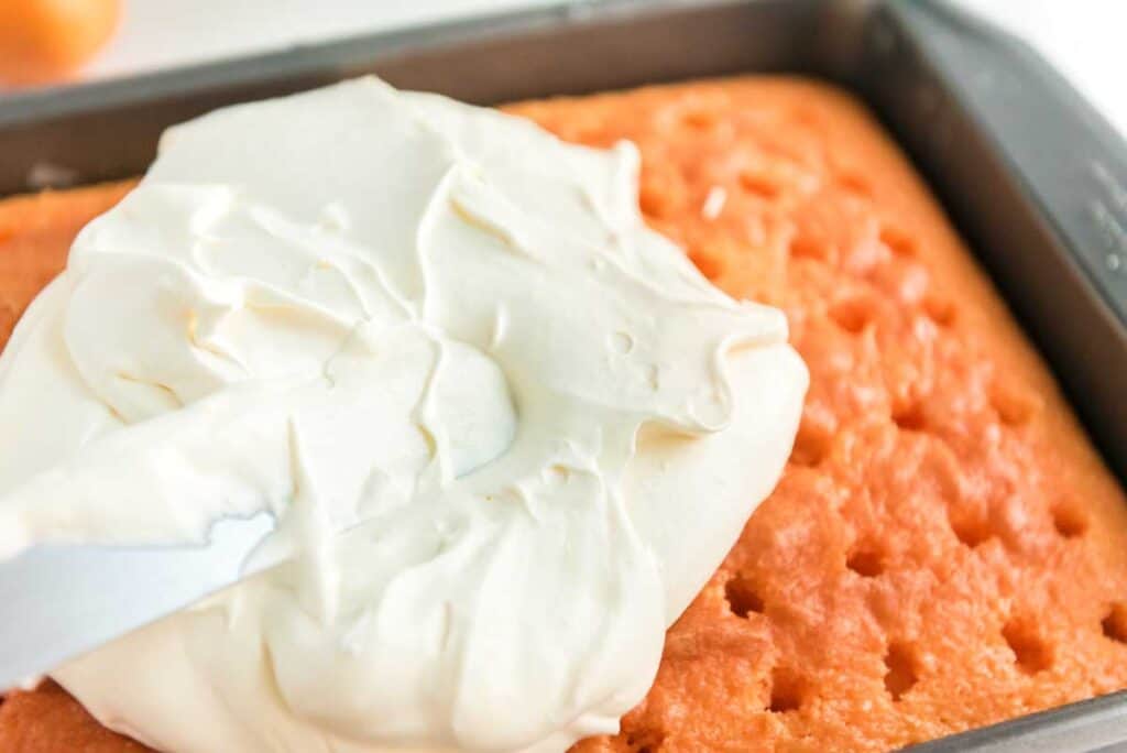 spreading whipped topping on orange creamsicle poke cake