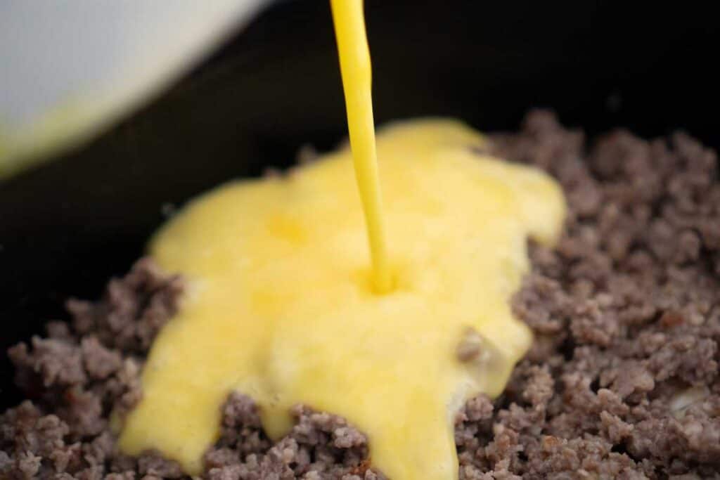 egg pouring over ground sausage