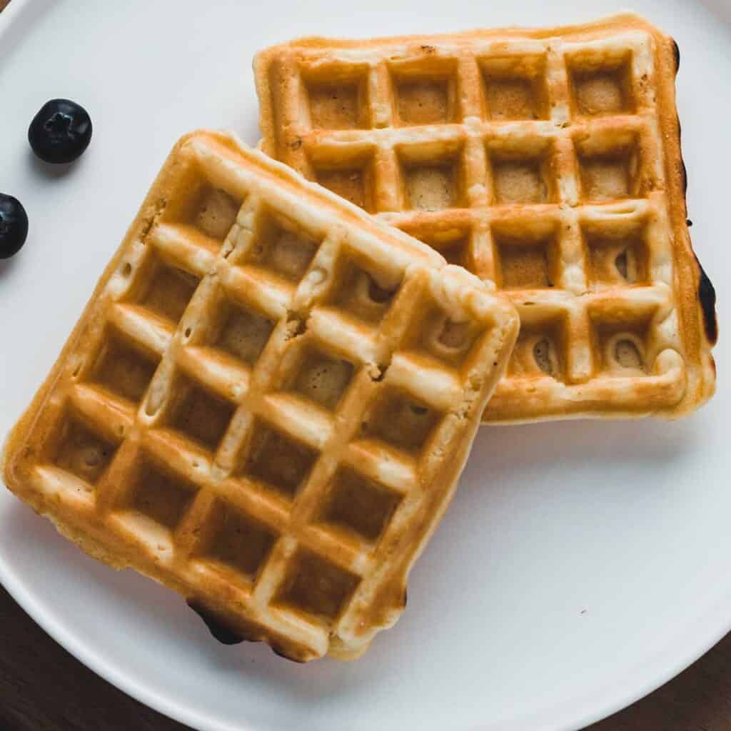 two cornbread waffles on a white plate with a few blueberries