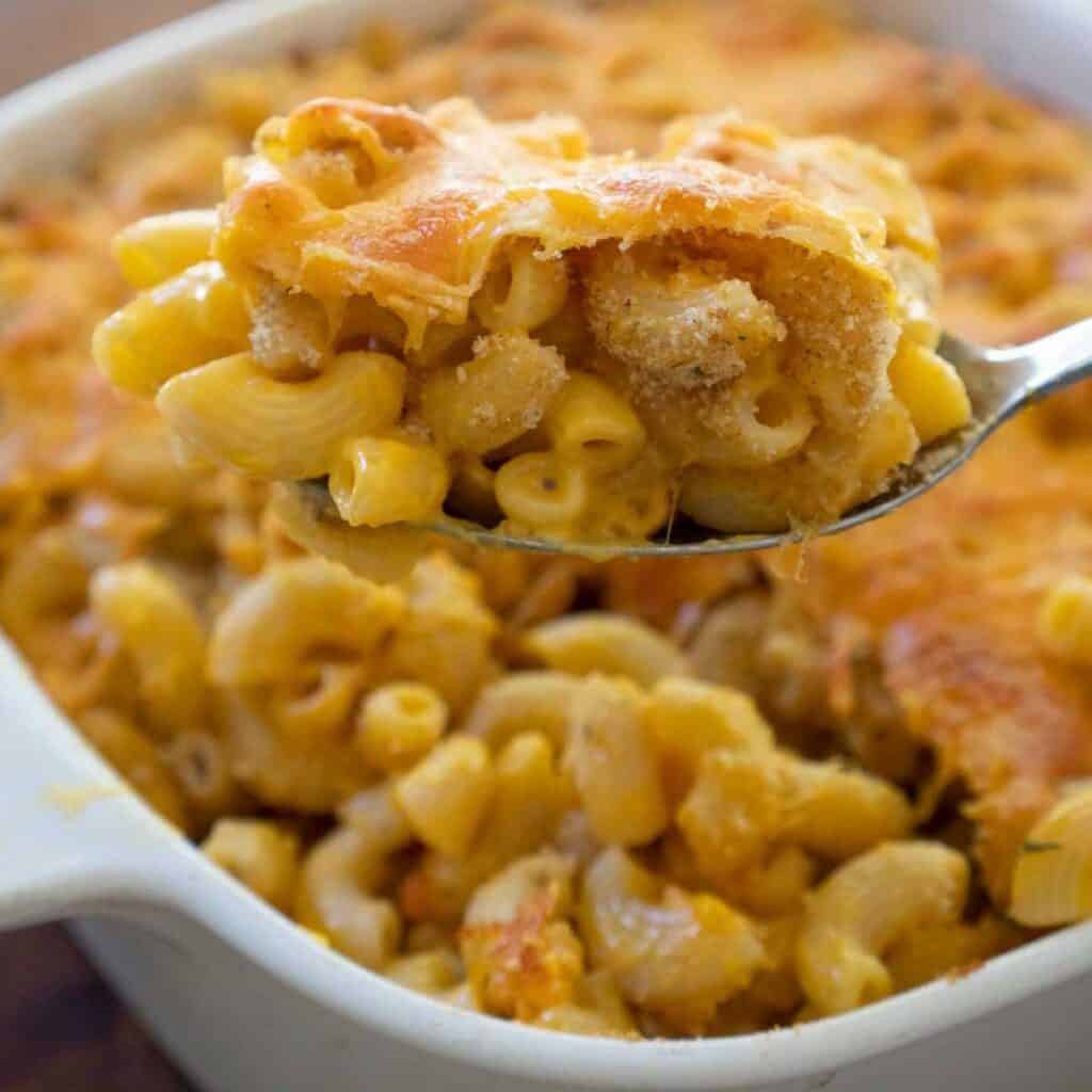 spoon holding scoop of baked box mac and cheese in baking dish