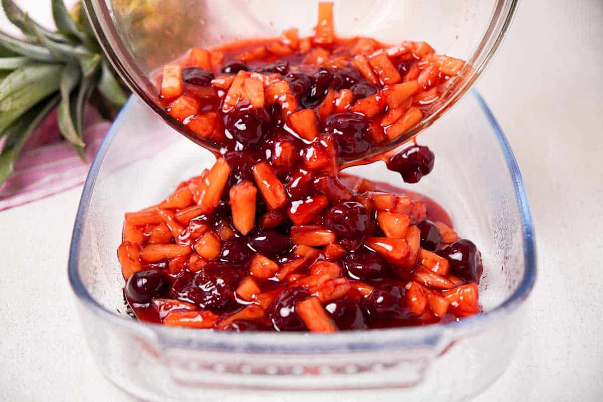pouring cherry pineapple dump cake filling into baking dish
