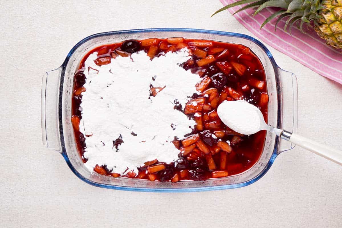 spooning cake mix over cherry pineapple dump cake