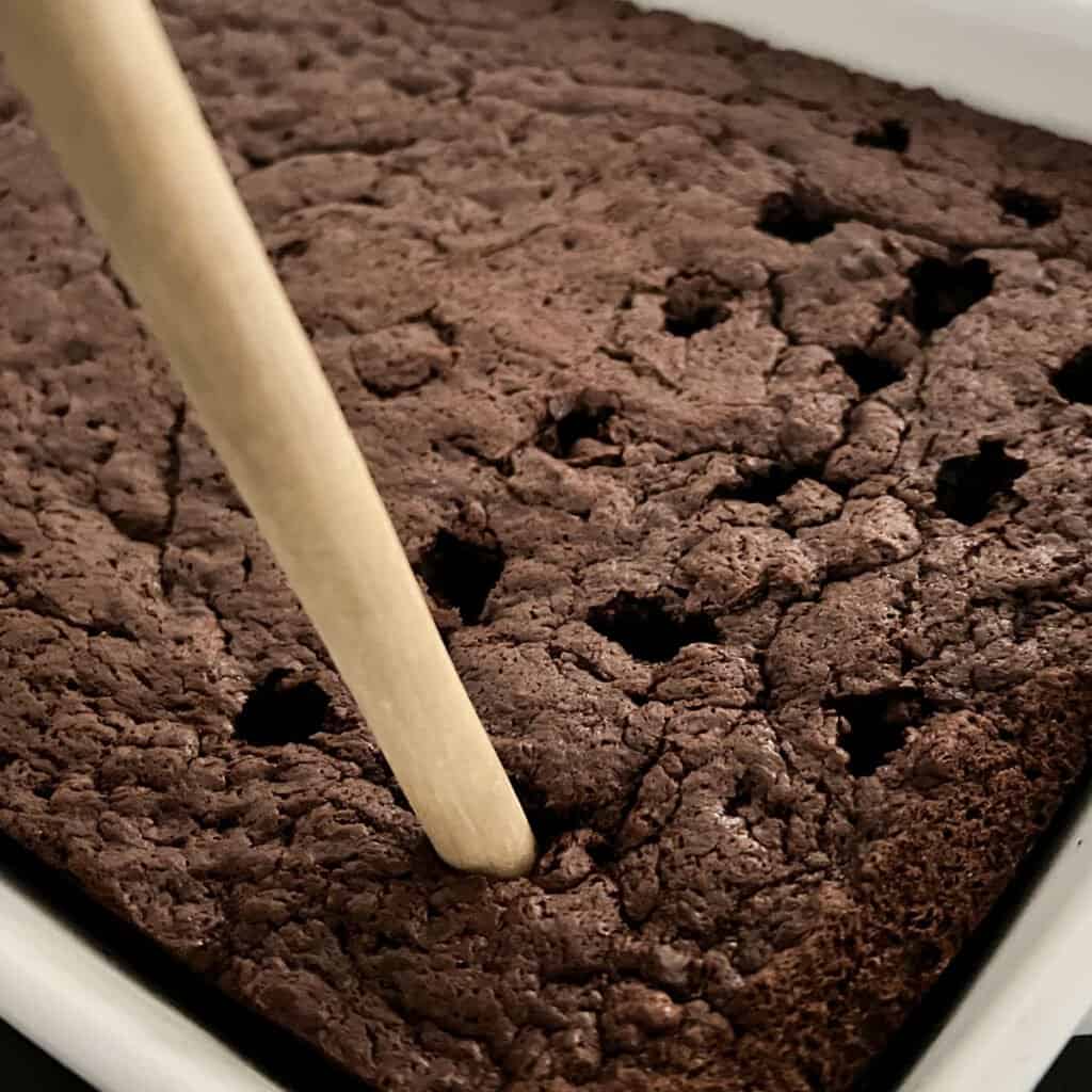 handle of wooden spoon poking holes in chocolate cake
