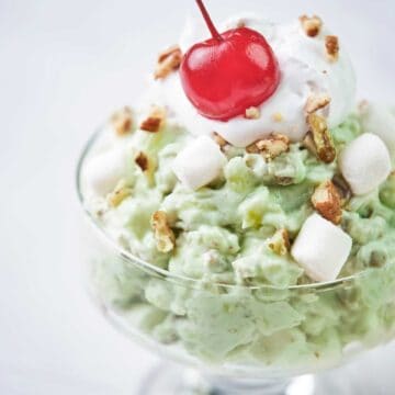close up of pistachio fluff in glass dish topped with a cherry