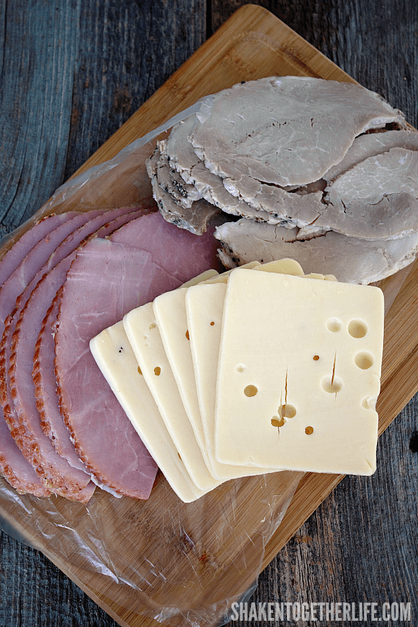 deli slice sweet ham, seasoned pork and swiss cheese in thick slabs on a cutting board
