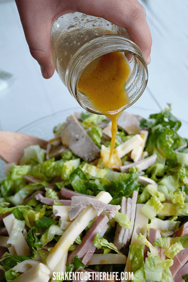 pouring a  tangy mustard vinaigrette on a hearty, low carb Cuban Cobb Salad!