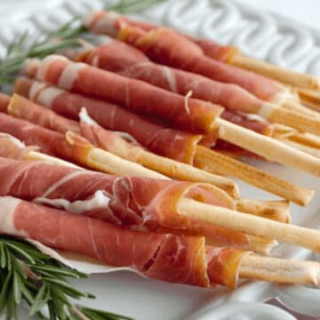 procuitto wrapped breadsticks on white plate