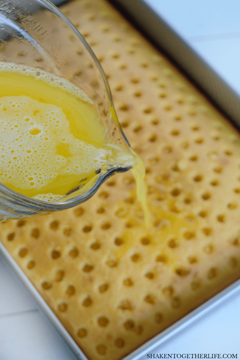 pouring lemon jello mix over poke cake