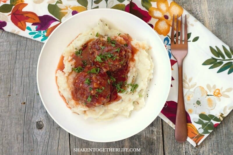 Porcupine Meatballs over mashed potatoes in white bowl with fork and napkin
