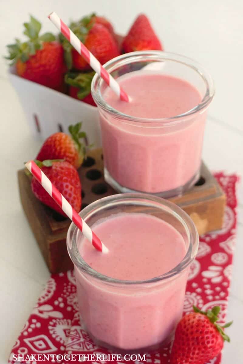 2 Frozen Strawberry Coladas with red and white striped paper straws and whole strawberries on red patterned napkin