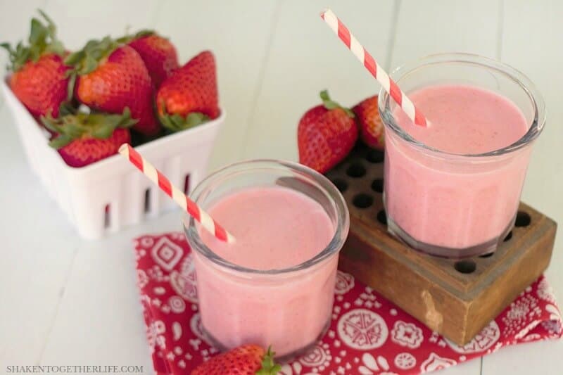 2 strawberry coladas with red and white striped straws and container of whole strawberries