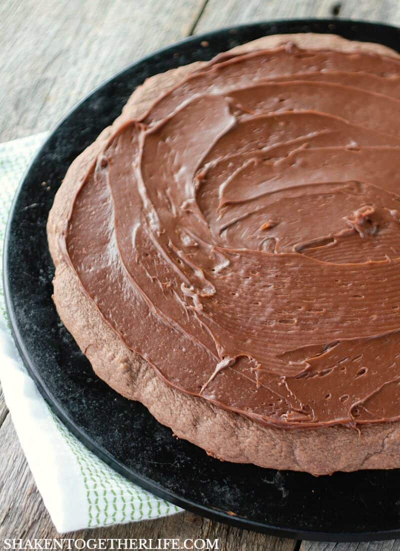 The brownie crust is spread with a generous layer of chocolate frosting in this Pumpkin Patch Dessert Pizza!