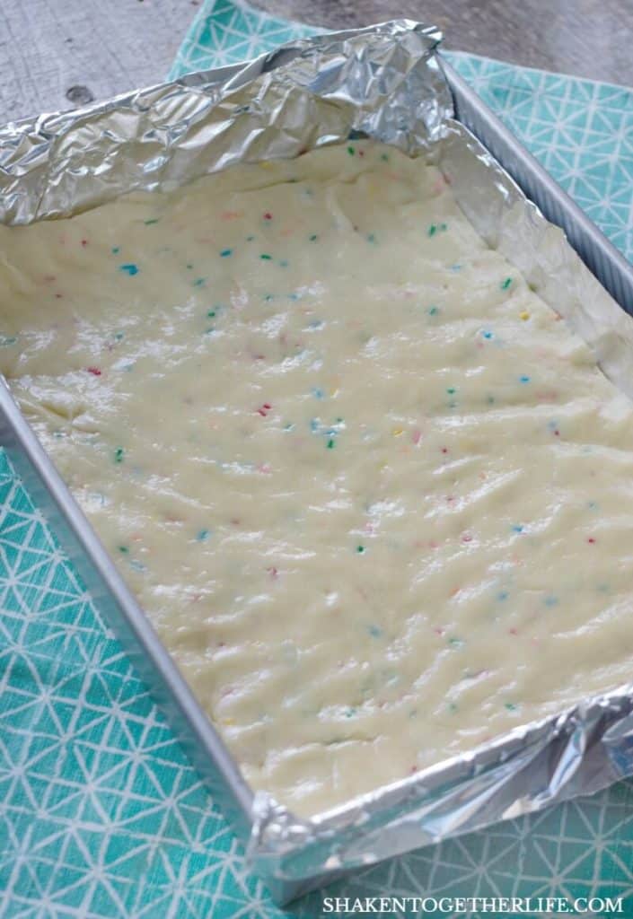 Funfetti Cookies Bars from a cake mix start by pressing the dough into a standard 9 x 13 cake pan lined with foil.