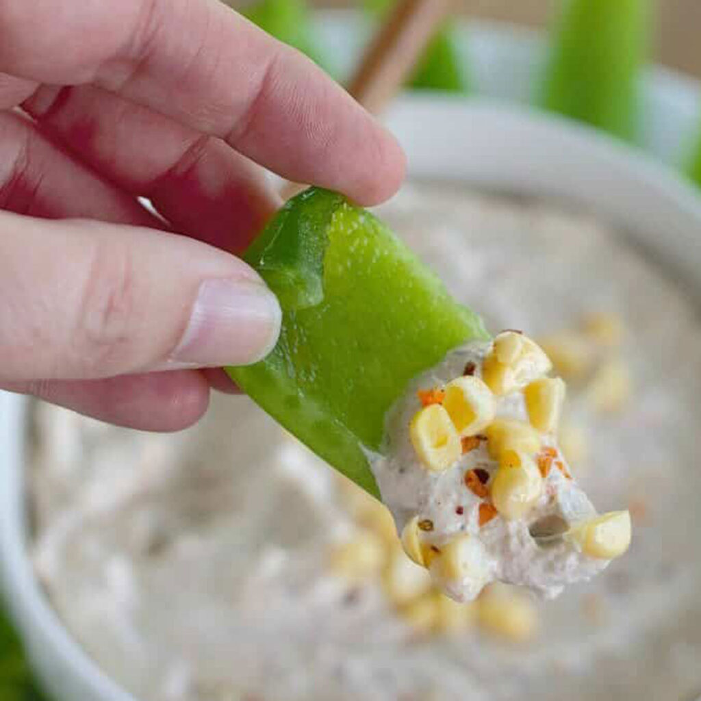 hand holding piece of green bell pepper with chipotle ranch dip on it