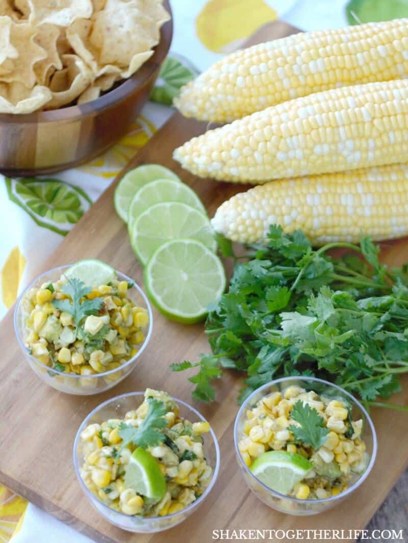 Corn & Avocado Salsa in three small bowls with corn bobs, sliced lime, and cilantro