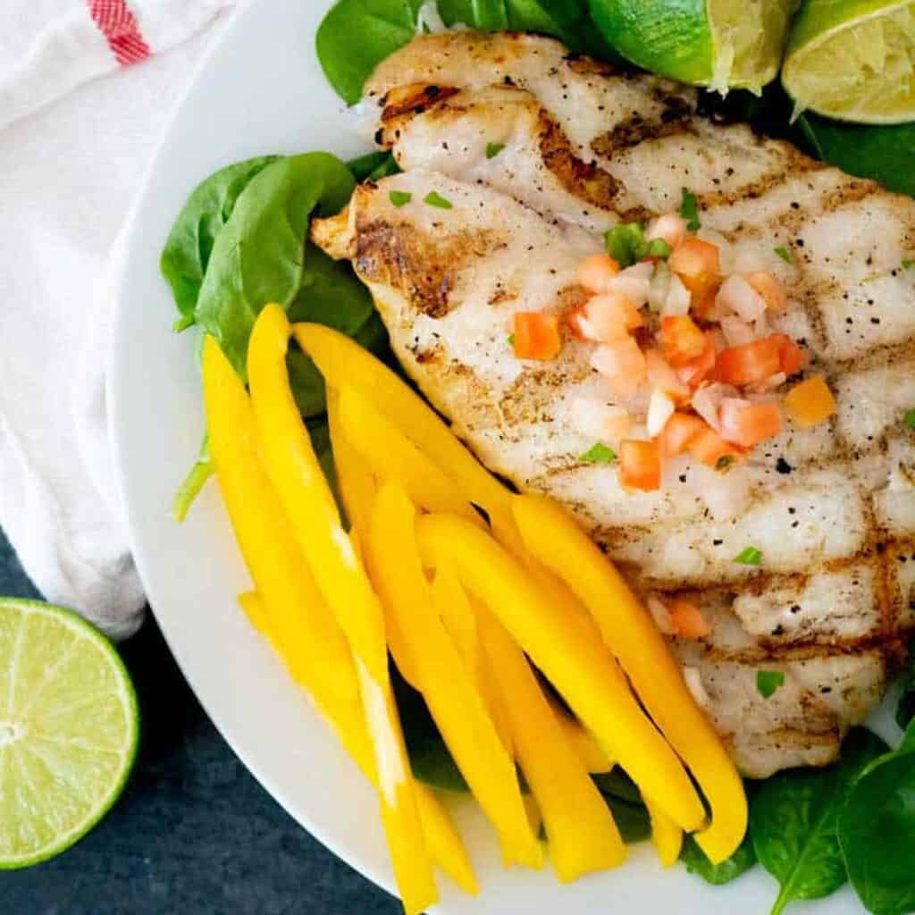 grilled grouper on plate with spinach and yellow bell pepper slices