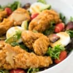 salad topped with crispy chicken strips in white bowl.