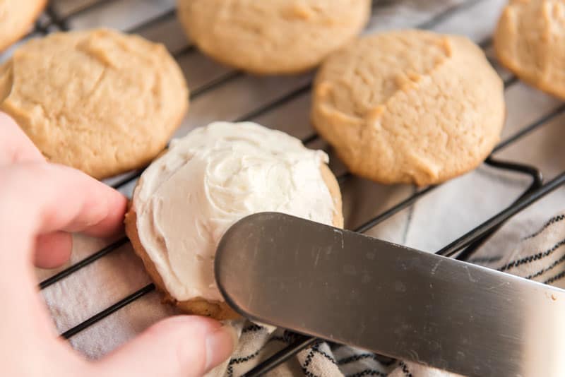spreading eggnog icing on cookie with spatula