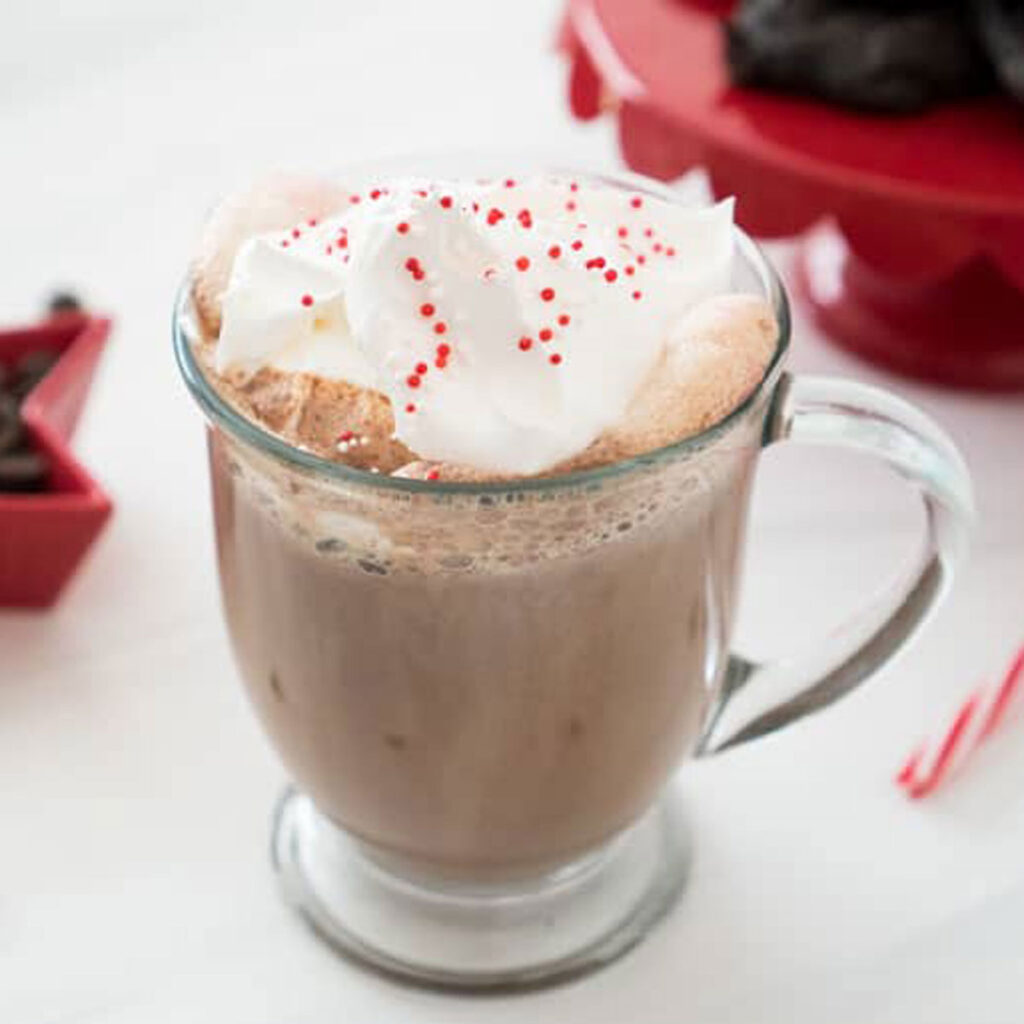glass mug with mint hot chocolate topped with whipped cream and sprinkles