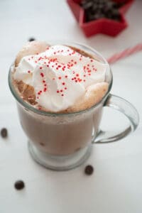 peppermint hot chocolate in glass mug with whipped cream and red and white sprinkles