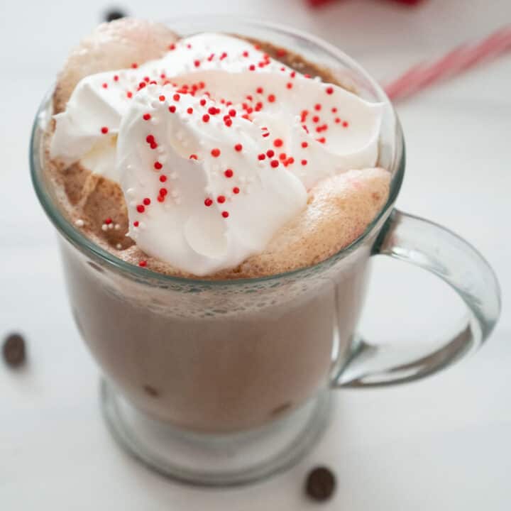 peppermint hot chocolate in glass mug with whipped cream and red and white sprinkles