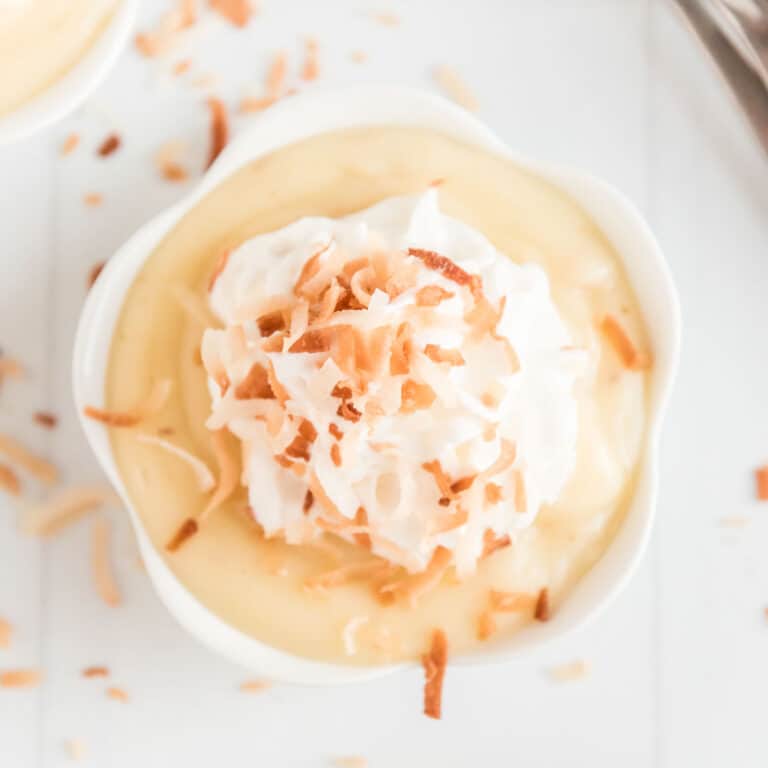 homemade coconut pudding in white ramekin with whipped cream and toasted coconut