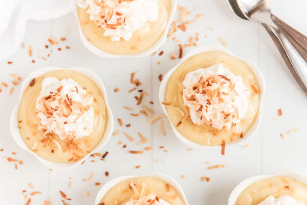 homemade coconut pudding in white ramekins with whipped cream and toasted coconut