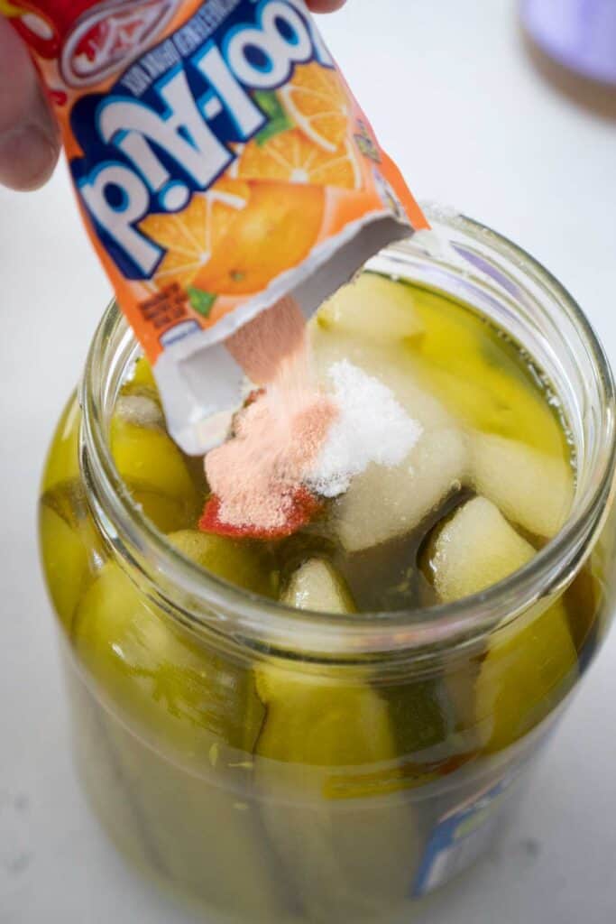 pouring packet of orange kool aid into pickle jar to make kool aid pickles