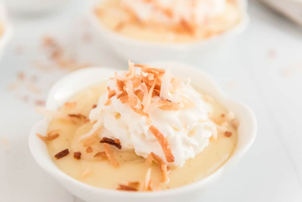 homemade coconut pudding in white ramekin with whipped cream and toasted coconut