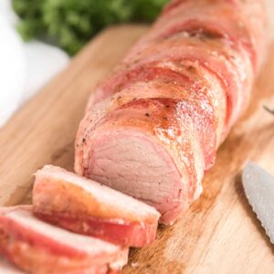bacon wrapped pork tenderloin on cutting board cut into medallions