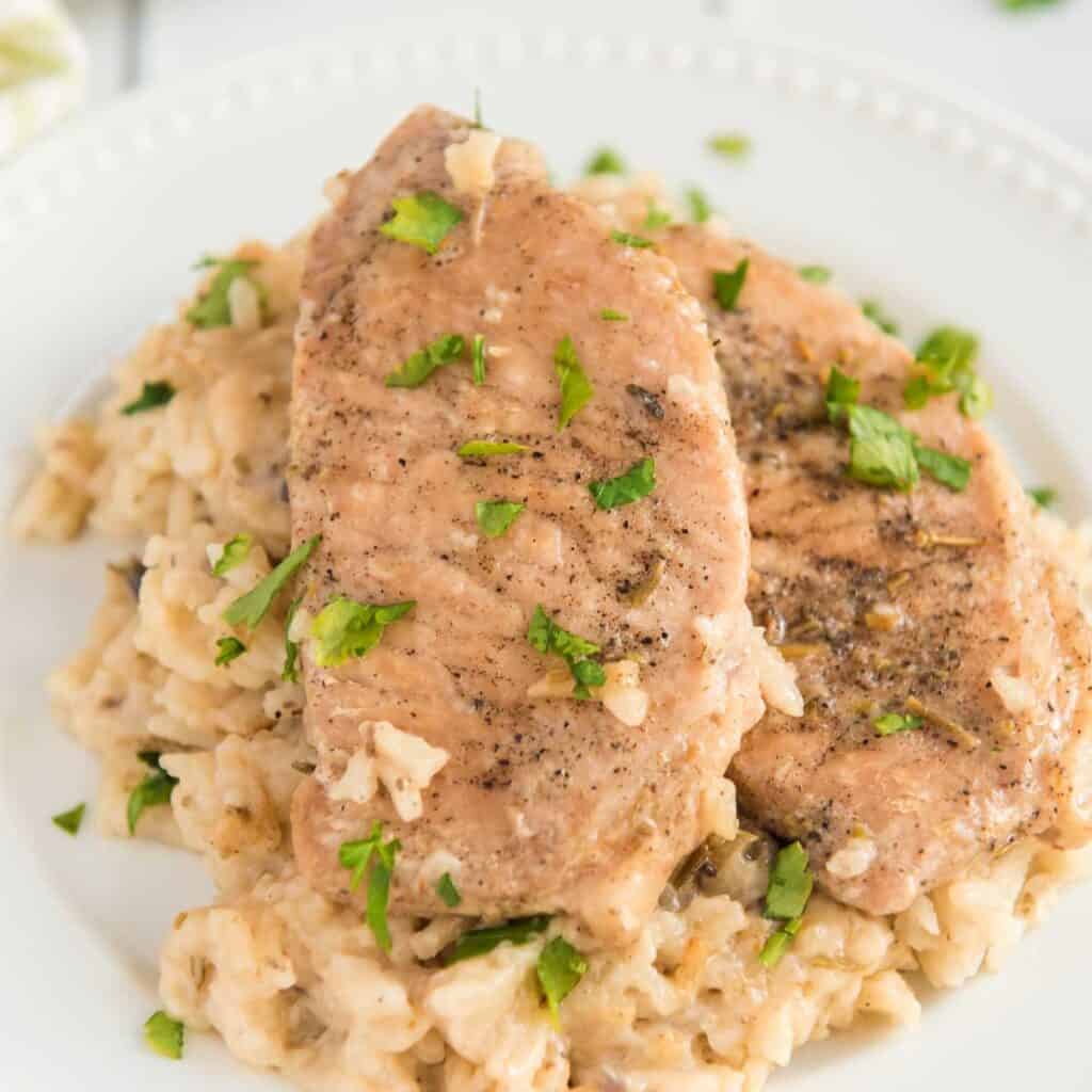 baked pork chops with mushroom rice on white plate with chopped parsley