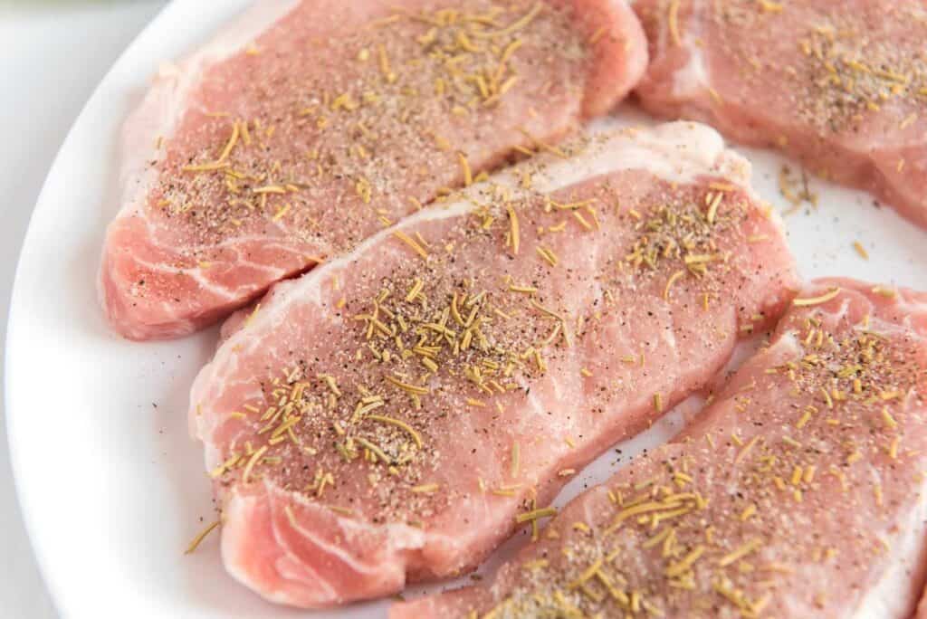 raw pork chops on white plate with herbs and seasonings