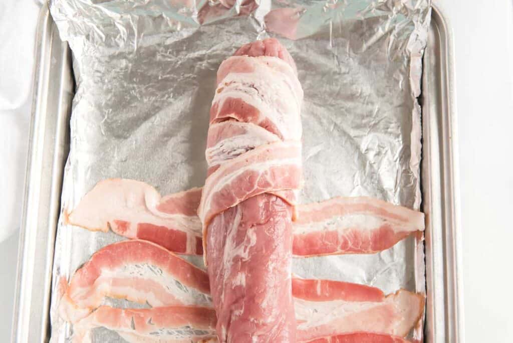 wrapping bacon around pork tenderloin on baking sheet