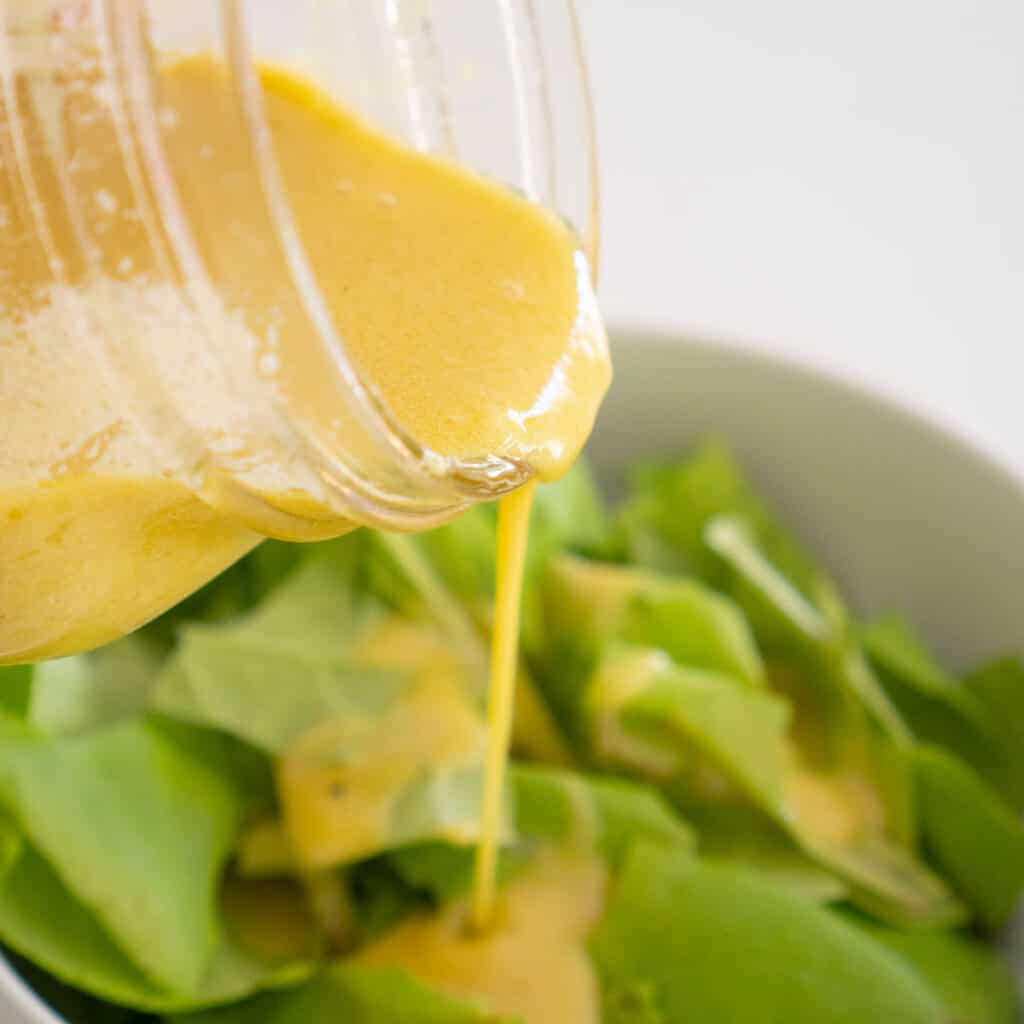 pouring homemade dijon vinaigrette over salad