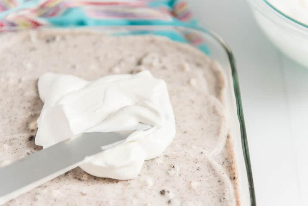 spreading whipped cream over oreo poke cake with spatula