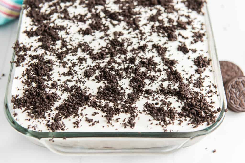 oreo poke cake in a glass casserole dish with whipped cream topped with oreo crumbles
