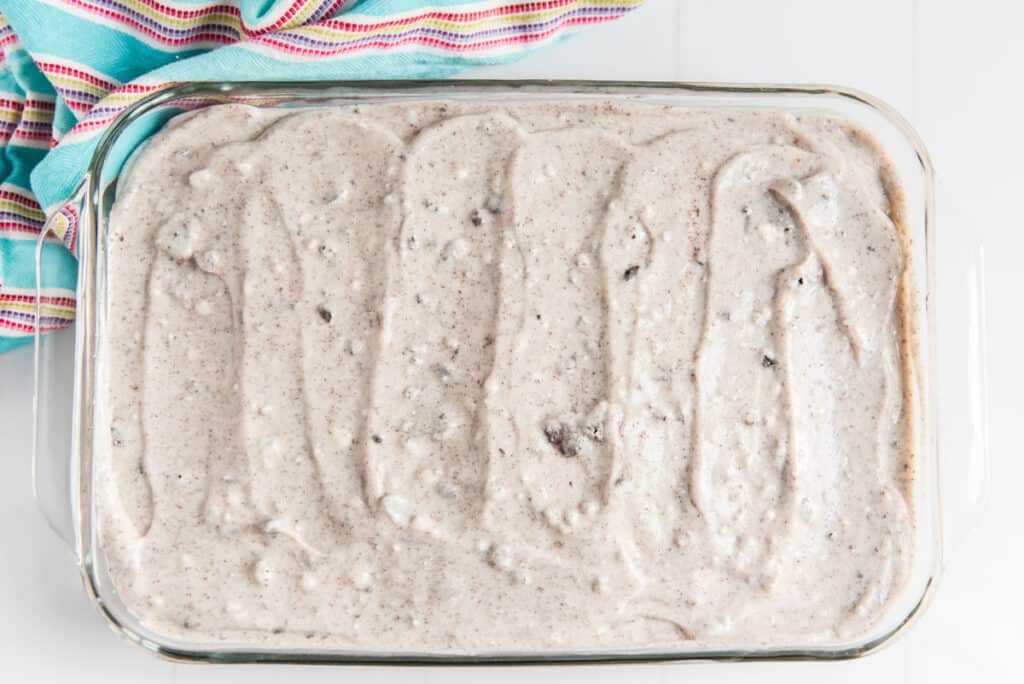 oreo poke cake with oreo pudding spread over the top in glass casserole dish with colorful towel