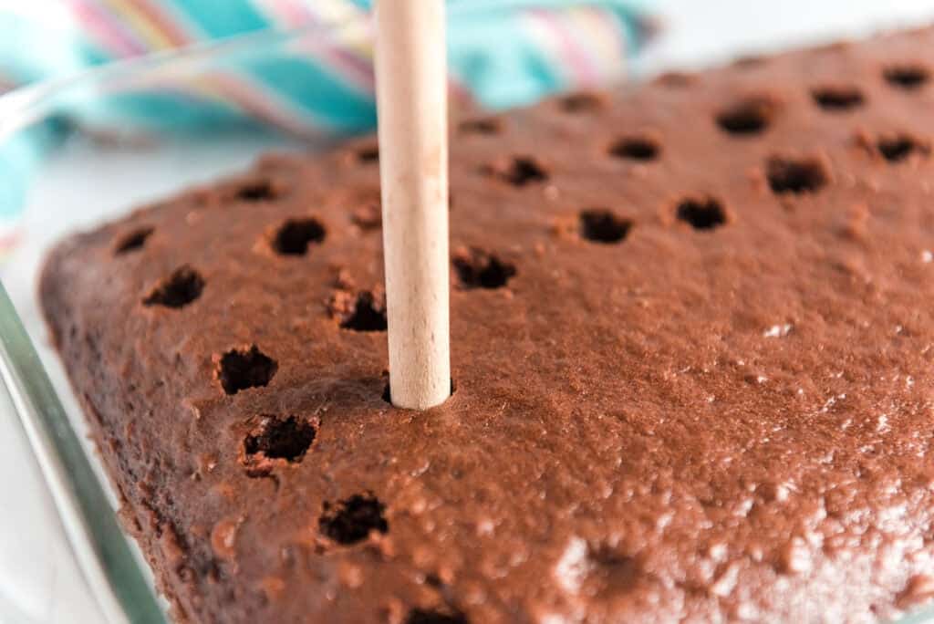poking holes in chocolate cake with wooden spoon to make oreo poke cake