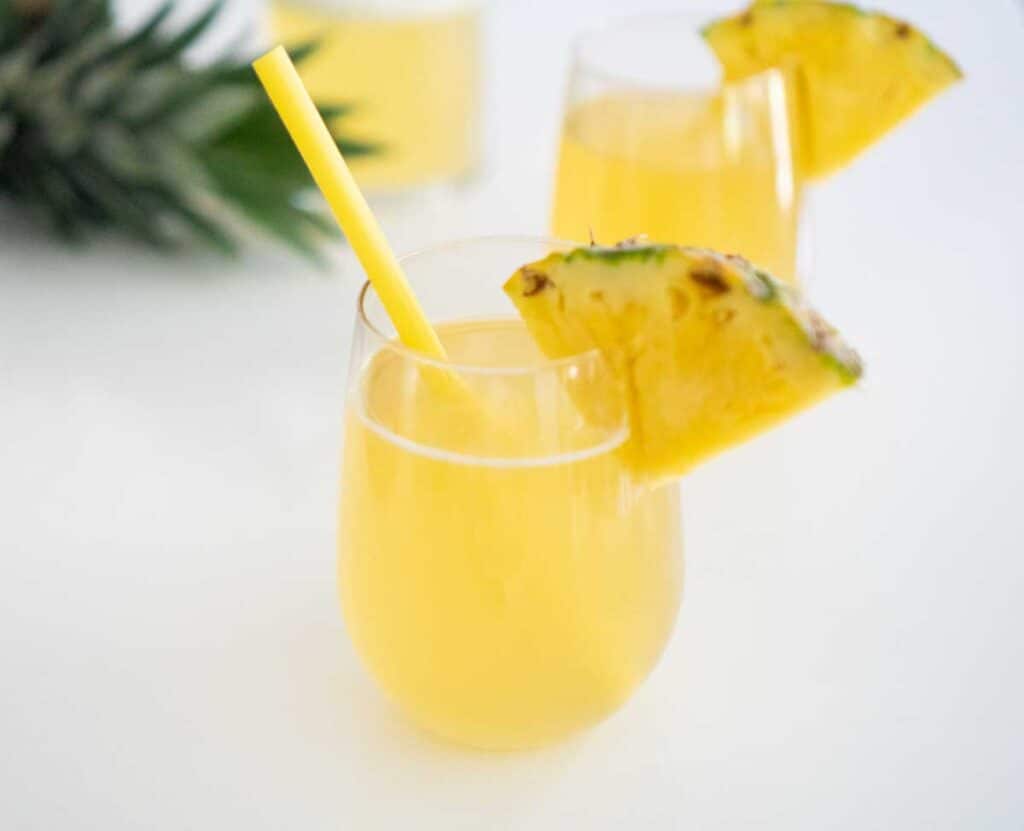 pineapple rum punch in stemless glass with slice of pineapple and yellow straw