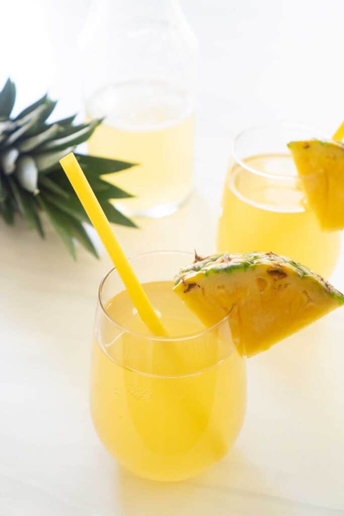 pineapple rum punch in stemless glass with slice of pineapple and yellow straw
