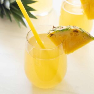 pineapple rum punch in stemless glass with slice of pineapple and yellow straw