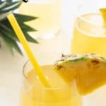 pineapple rum punch in stemless glass with slice of pineapple and yellow straw