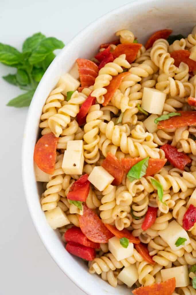 overhead view of italian pasta salad in white bowl with basil sprig nearby