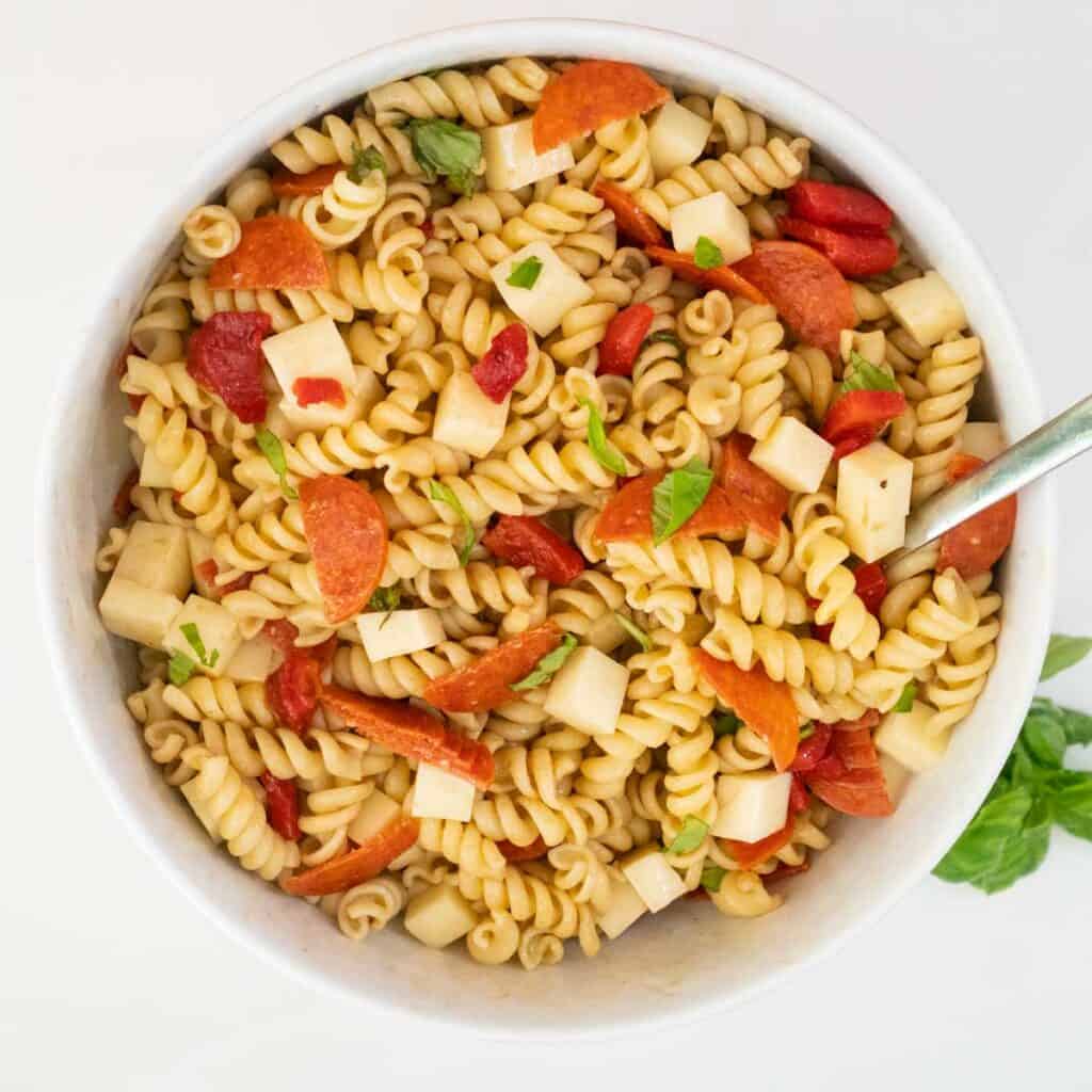 Italian pasta salad in a white bowl with a basil sprig nearby