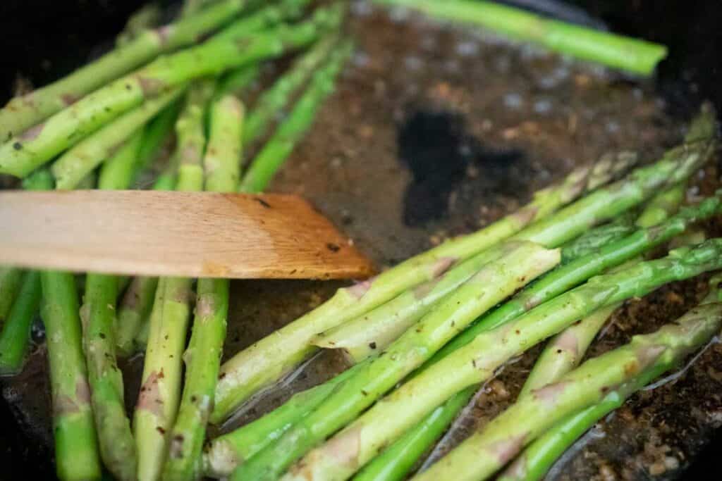 wooden spatula deglazing pan with asparagus and broth