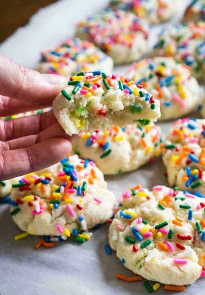 hand holding funfetti cookie with bite taken out with more cookies in background