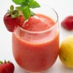 frozen strawberry lemonade in a stemless wine glass with strawberry and mint garnish