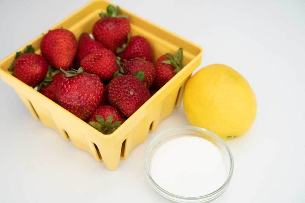 carton of strawberries, lemon, and small glass bowl of sugar