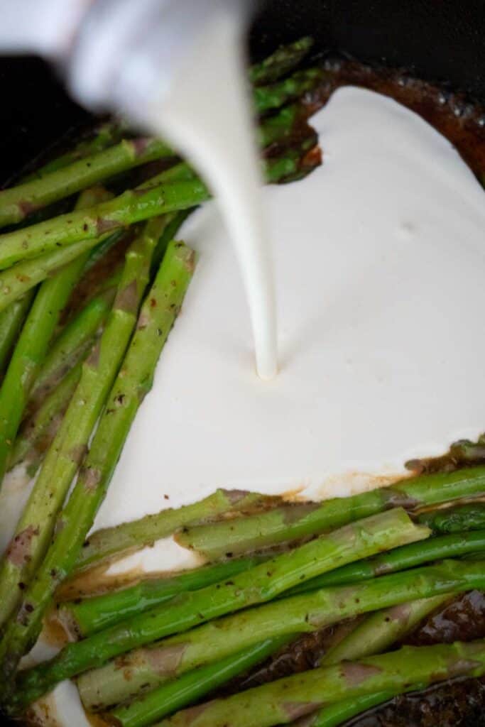 cream pouring into pan with asparagus