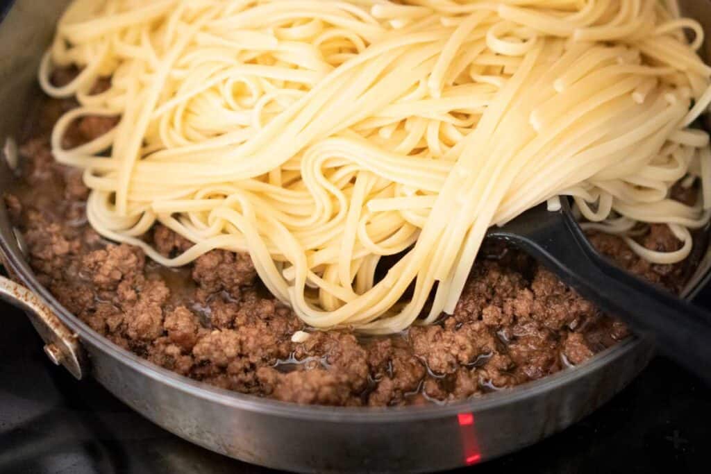 adding noodles to ground beef in pan